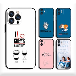 May include: Five phone cases with Grey's Anatomy themes. One white case features a coffee cup, wine glass, and text. Four smaller cases in blue and pink feature anatomical heart illustrations, cartoon characters, and text including You're My Person.