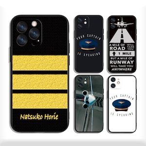 May include: A collection of black phone cases with various designs. One case features yellow stripes and the name "Natsuko Horie." Other cases display aviation-themed graphics, including a pilot's hat and the text "Your Captain Is Speaking."