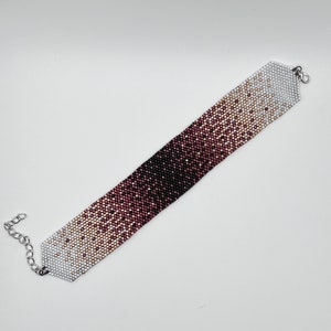 May include: A beaded bracelet with a gradient of colors from white to black, with a silver clasp.