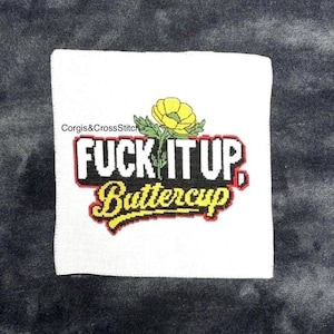 Op de afbeelding: Wit kruissteektextiel met de tekst "FUCK IT UP, Buttercup" in zwart, rood en geel. Boven de tekst staat een gele bloem met groene bladeren. De tekst "Corgis&CrossStitch" staat in de linkerbovenhoek.