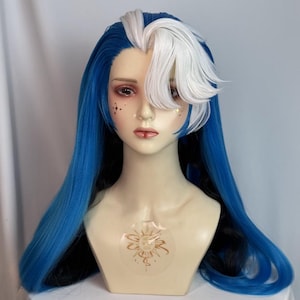 Può includere: Una testa di manichino che indossa una parrucca lunga e liscia con capelli blu vibranti e una sezione bianca prominente sulla parte anteriore. Il manichino ha pelle chiara, occhi scuri, adesivi facciali dorati a stella e un emblema solare dorato.