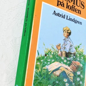 Puede incluir: Un libro verde y naranja con el t&iacute;tulo "Rasmus p&aring; loften" de Astrid Lindgren. La portada presenta una ilustraci&oacute;n de un ni&ntilde;o sentado en un campo de flores, mirando hacia el cielo.