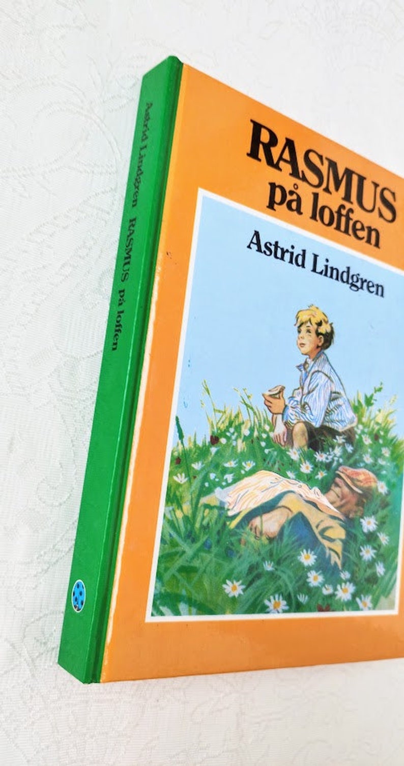 Puede incluir: Un libro verde y naranja con el t&iacute;tulo "Rasmus p&aring; loften" de Astrid Lindgren. La portada presenta una ilustraci&oacute;n de un ni&ntilde;o sentado en un campo de flores, mirando hacia el cielo.