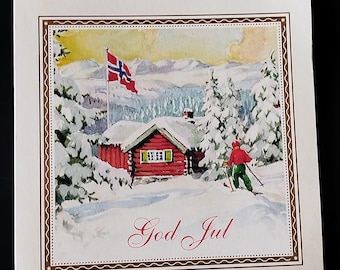 May include: A square greeting card featuring a watercolor illustration of a red log cabin in a snowy landscape with a Norwegian flag, a skier in red and green, and the text God Jul written in red script at the bottom within a decorative border.