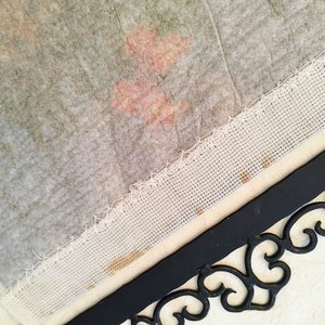 May include: A close-up of a white fabric with a decorative border. The fabric is attached to a black metal frame with a decorative scroll design.