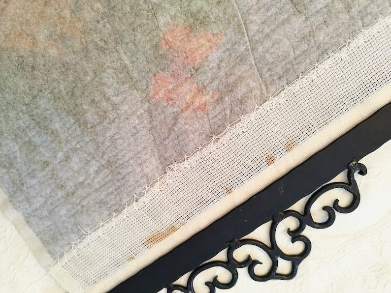 May include: A close-up of a white fabric with a decorative border. The fabric is attached to a black metal frame with a decorative scroll design.