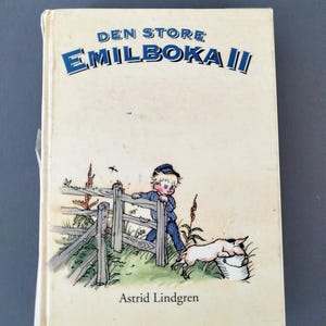 Può includere: Un libro per bambini vintage intitolato "DEN STORE EMILBOKA II" di Astrid Lindgren. La copertina presenta un ragazzo in abiti blu appoggiato a una staccionata di legno, con un maiale e un secchio. Il libro ha una copertina color crema.