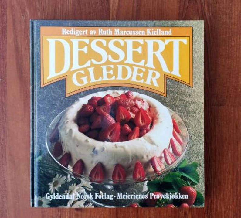 Puede incluir: Un libro de cocina amarillo con el t&iacute;tulo "Dessert Gleder" y una imagen de un postre blanco cubierto de fresas en un plato blanco.