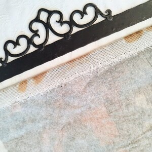 May include: A white fabric with brown stains along the edge, attached to a black metal frame with a decorative design.