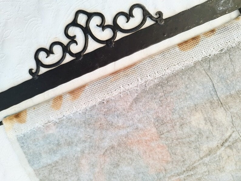 May include: A white fabric with brown stains along the edge, attached to a black metal frame with a decorative design.