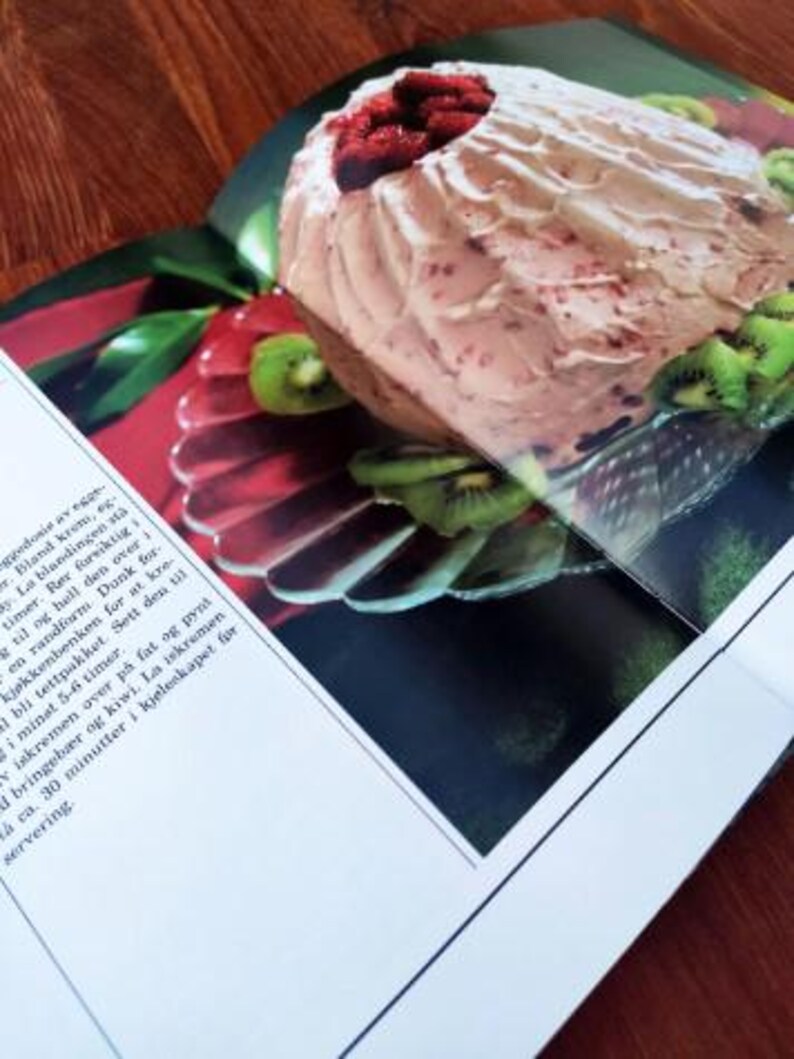 Puede incluir: Un postre rosa y blanco con relleno de frambuesa, cubierto con frambuesas frescas y rodajas de kiwi. El postre est&aacute; en un plato blanco con un borde plateado.