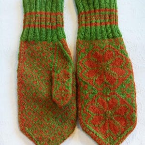 May include: A pair of knitted mittens in shades of green and orange. The cuffs are green with orange stripes, and the body features a repeating pattern of orange floral designs on a green background. The mittens are designed for warmth and comfort.