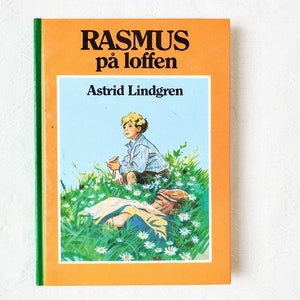 Puede incluir: Un libro infantil vintage titulado "Rasmus p&aring; loften" de Astrid Lindgren. La portada presenta una ilustraci&oacute;n de dos ni&ntilde;os en un campo de flores. Un ni&ntilde;o est&aacute; sentado en el suelo, mientras que el otro est&aacute; acostado.