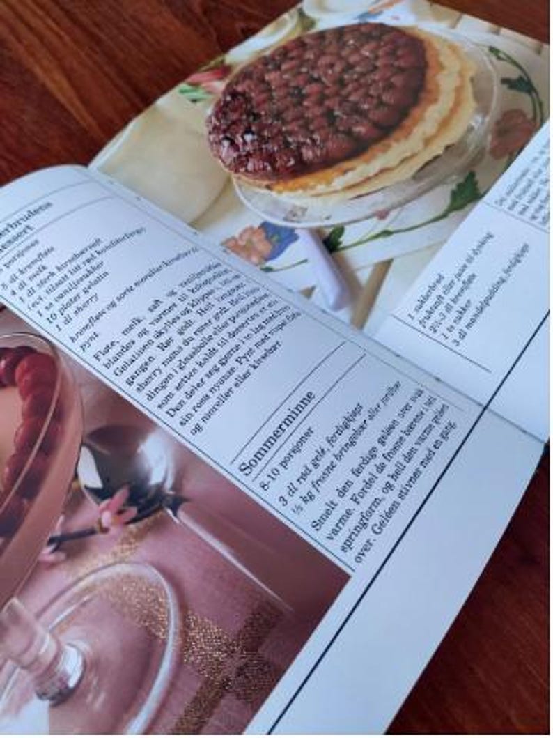 Puede incluir: Un primer plano de una p&aacute;gina de un libro de recetas con una foto de un postre. El postre es una tarta con un relleno marr&oacute;n y una corteza dorada. El texto de la p&aacute;gina est&aacute; en un idioma escandinavo e incluye las palabras "Sommerminne" y "8-10 porsjoner".