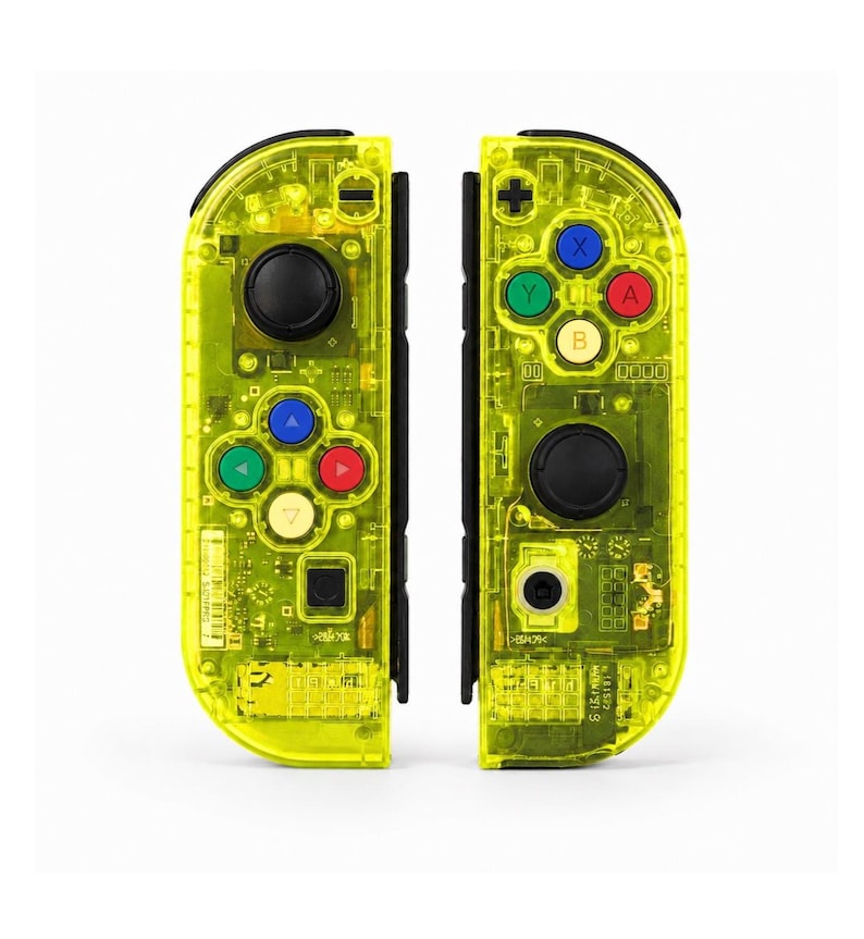 May include: A pair of neon yellow transparent game controllers featuring black joysticks and buttons in red, blue, green, and yellow. The internal electronic components are visible through the clear casing, including various buttons and directional pads.