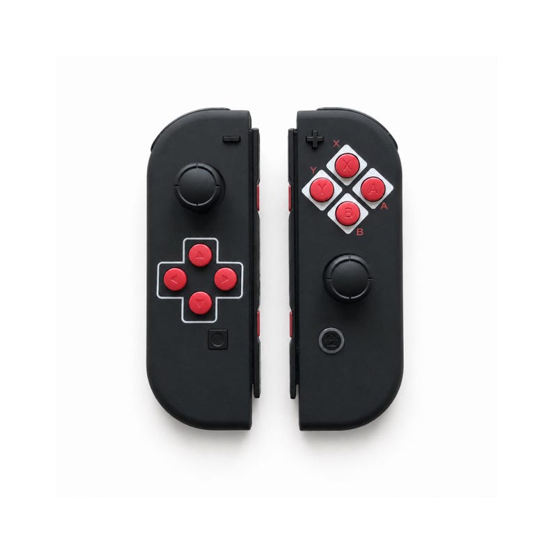 Pode incluir: Dois controles de jogo pretos com bot&otilde;es vermelhos e brancos. Cada controle tem um joystick e um conjunto de bot&otilde;es. Os controles s&atilde;o projetados para um console de jogos e s&atilde;o mostrados em um fundo branco.