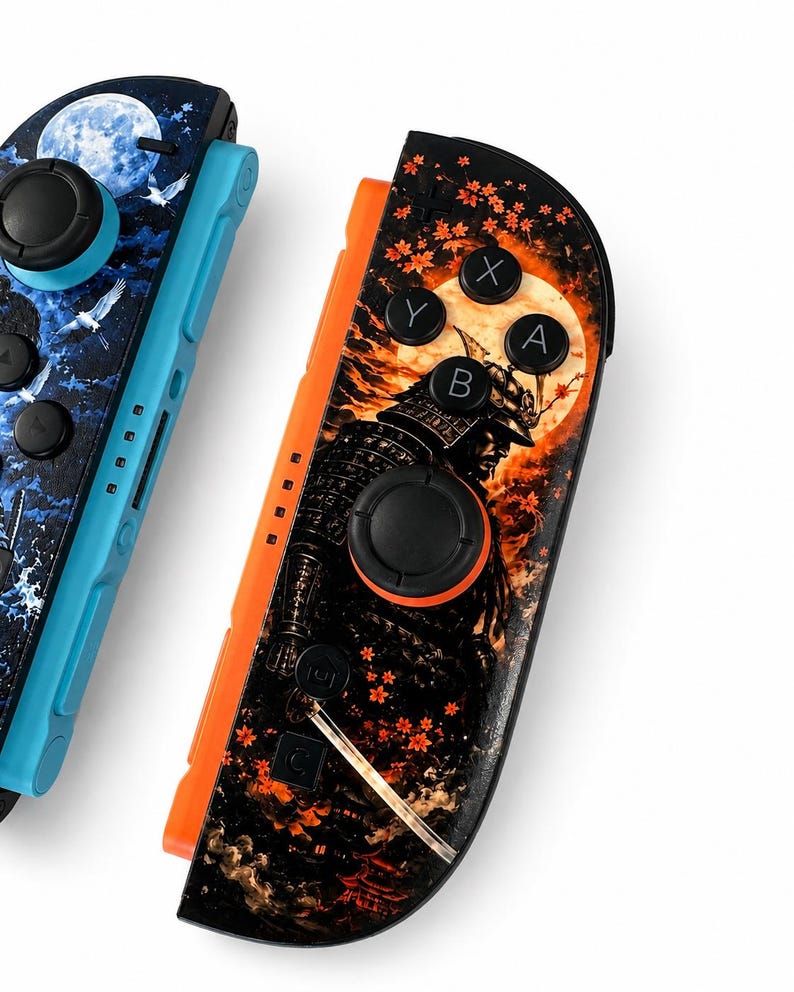 May include: Two game controllers featuring custom graphic skins. The left controller is light blue with a dark blue night sky, moon, and bird design. The right controller is orange with a black samurai, orange moon, and red maple leaf pattern.