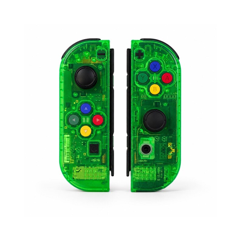 May include: Two transparent green game controllers with black buttons and colored directional buttons. The controllers are designed with a clear casing, revealing the internal components. The controllers are shown against a white background.