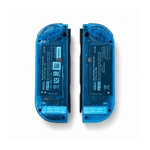 Pu&ograve; includere: Due controller di gioco blu trasparenti, ciascuno con una cornice nera. I controller rivelano i componenti interni attraverso la plastica blu. Testo e simboli sono stampati sul retro di ogni controller, tra cui "RECHARGEABLE LI-ION BATTERY".