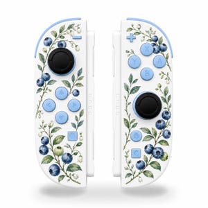 May include: A pair of white game controllers featuring a watercolor-style botanical print of blue blueberries, green leaves, and small white flowers. The controllers include light blue buttons, a directional pad, and black joysticks.