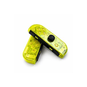 May include: Two video game controllers with a translucent neon yellow shell. Each controller features a black analog stick, a directional pad, four circular action buttons, and additional small function buttons. The internal electronic components are visible through the clear yellow plastic casing.