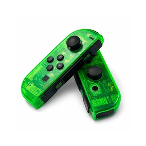 May include: Two transparent green game controllers with black buttons and joysticks are displayed against a white background. The controllers are angled, showing their internal circuitry. The controllers are designed for a gaming console.