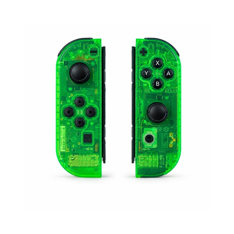 May include: Two neon green game controllers with black buttons and directional pads. The controllers have a transparent design, revealing internal components. The controllers are designed for a gaming console.