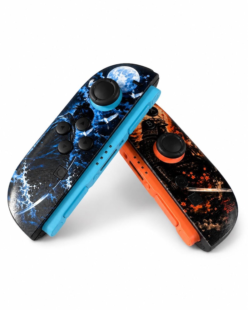 May include: Two game controllers featuring custom graphic skins. The left controller has a blue base with a moon, waves, and bird design. The right controller has an orange base with a samurai figure, sword, and red floral accents.