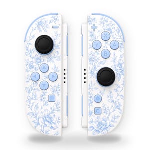 May include: A pair of video game controllers featuring a white base with a light blue floral pattern. The left controller has a black joystick and light blue directional buttons. The right controller has a black joystick and light blue A, B, X, Y buttons.