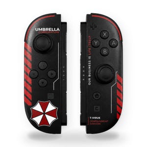 May include: A pair of black video game controllers featuring red diagonal stripes and the Umbrella Corporation logo. The left controller displays the text UMBRELLA CORPORATION, while the right controller features the text OUR BUSINESS IS LIFE ITSELF and T-VIRUS CONTAINMENT DIVISION.
