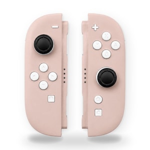 May include: A pair of pastel pink video game controllers featuring black analog sticks and white buttons. The left controller includes a directional pad and a minus button, while the right controller has A, B, X, Y buttons, a plus button, and home icons.