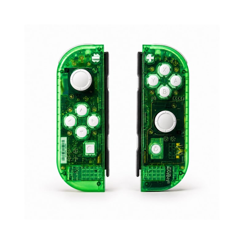 May include: Two transparent green game controllers with white buttons and black accents. The controllers have visible internal circuitry and are designed for a gaming console. The buttons are labeled with letters and symbols.