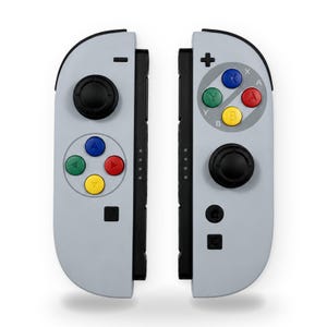 Könnte beinhalten: Ein Paar hellgraue Videospiel-Controller mit schwarzen Joysticks und Tasten. Der linke Controller hat ein Steuerkreuz mit blauen, grünen, roten und gelben Tasten. Der rechte Controller verfügt über A-, B-, X- und Y-Tasten in denselben Farben.