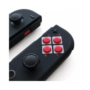 Pode incluir: Dois comandos de jogo pretos com bot&otilde;es e joysticks vermelhos. Os comandos t&ecirc;m um design elegante com um acabamento fosco. Os bot&otilde;es s&atilde;o rotulados com letras e s&iacute;mbolos.