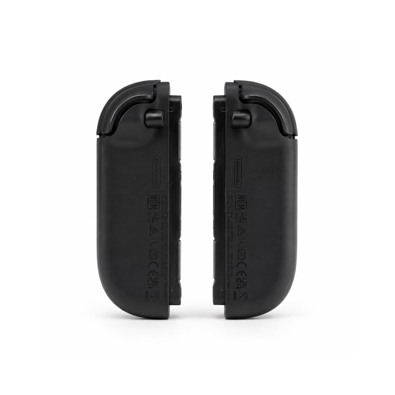 May include: Two black gaming controller attachments with rounded top edges and flat side profiles. Each unit features a small protruding button near the top and various regulatory markings and text printed vertically along the side surface.