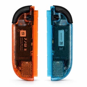 May include: A pair of video game controllers featuring a translucent orange shell on the left and a translucent blue shell on the right. Both controllers have black top buttons and internal components visible through the casing, including printed text and QR codes.
