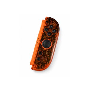 May include: A right-side video game controller featuring a translucent orange plastic shell that reveals internal electronic components. The device includes a black circular joystick, four action buttons labeled A, B, X, and Y, and two smaller buttons.