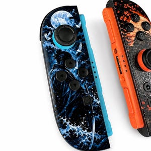 May include: Two game controllers featuring custom graphic skins. The left controller displays a blue-toned scene with a samurai, a full moon, and crashing waves. The right controller features an orange-toned design with autumn leaves and a moon.