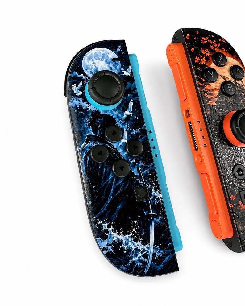 May include: Two game controllers featuring custom graphic skins. The left controller displays a blue-toned scene with a samurai, a full moon, and crashing waves. The right controller features an orange-toned design with autumn leaves and a moon.