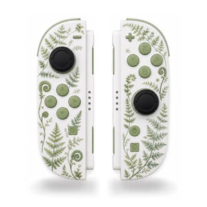 May include: A pair of white video game controllers featuring a green fern leaf pattern. The left controller has a black joystick and green directional buttons, while the right controller has a black joystick and green A, B, X, Y buttons.