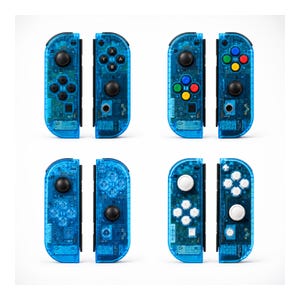 Pu&ograve; includere: Quattro paia di controller di gioco blu trasparenti. Ogni controller ha un diverso layout di pulsanti, con pulsanti neri, bianchi e colorati. I controller sono progettati per una console di gioco e sono visualizzati su uno sfondo bianco.