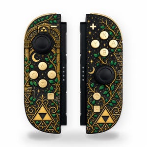 Puede incluir: Un par de mandos de juego negros con ilustraciones botánicas en dorado y verde, símbolos Triforce dorados, lunas crecientes y estrellas. Los mandos incluyen botones dorados con flechas direccionales, letras e iconos sobre un fondo oscuro.