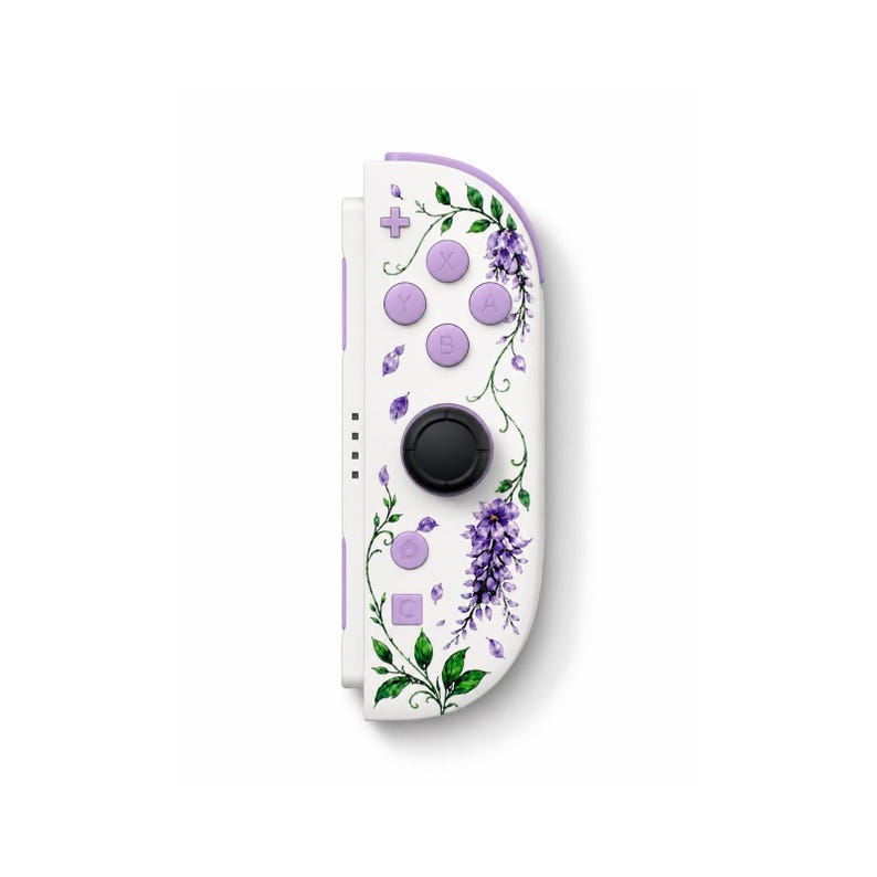 Puede incluir: Un mando de videoconsola tipo joy-con de color blanco con un estampado floral de glicinias moradas y hojas verdes. El dispositivo incluye un joystick circular negro, cuatro botones de acci&oacute;n morados con las letras X, Y, A y B, un bot&oacute;n m&aacute;s y dos botones inferiores.