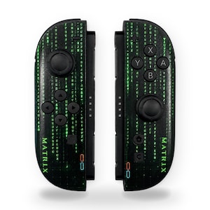 May include: Two black game controllers featuring a green digital code pattern and the word MATRIX printed in green. The controllers include black joysticks, directional buttons, and action buttons labeled A, B, X, and Y, with small blue and orange indicator lights.