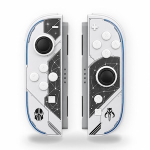 May include: A pair of white and black game controllers featuring a space-themed graphic with star patterns, a black joystick, white buttons, and two distinct black helmet-shaped icons printed on the lower sections of each controller.
