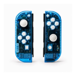Pu&ograve; includere: Due controller di gioco blu trasparenti con componenti interni visibili. Ogni controller ha pulsanti bianchi e un joystick. I controller sono progettati per una console di gioco e sono su uno sfondo bianco.