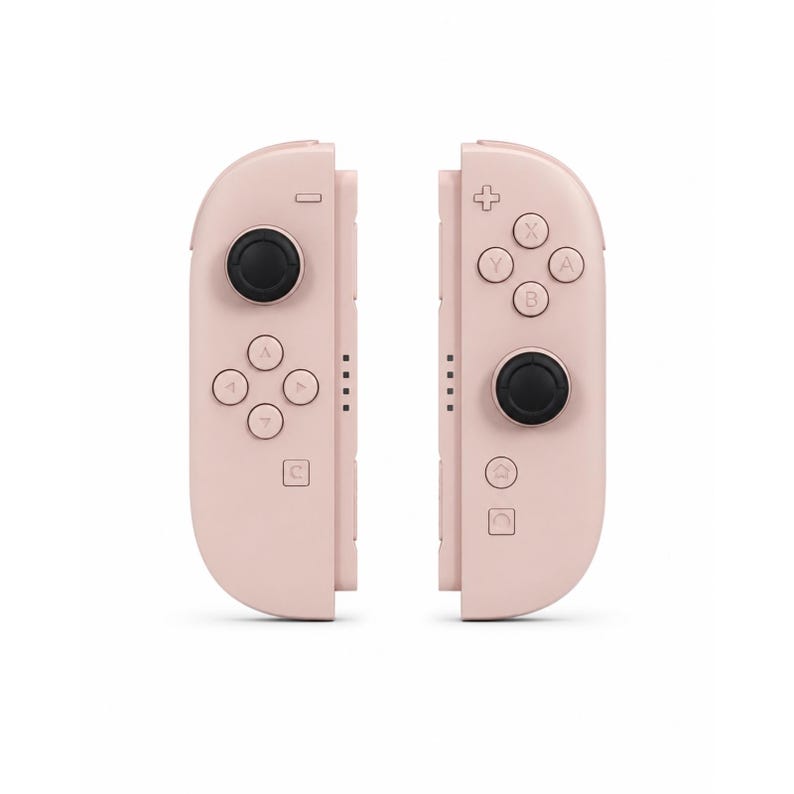 May include: A pair of pastel pink video game controllers featuring black analogue sticks. The left controller has a directional pad and a minus button, while the right controller includes four action buttons, a plus button, and home icons.
