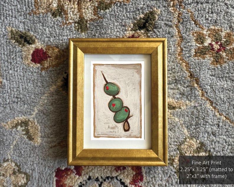 May include: A framed art print of a green olive branch with red accents on a white background. The print is matted to 2 inches by 3 inches and framed in a gold frame.