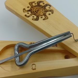 May include: A wooden box with a sun design on the lid, containing a metal tongue drum. The box is labeled "C3".