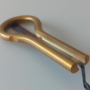 May include: A gold-coloured metal musical instrument called a 'thumb piano' or 'kalimba'. It has a curved shape with a single string and a metal arm that vibrates to create sound.